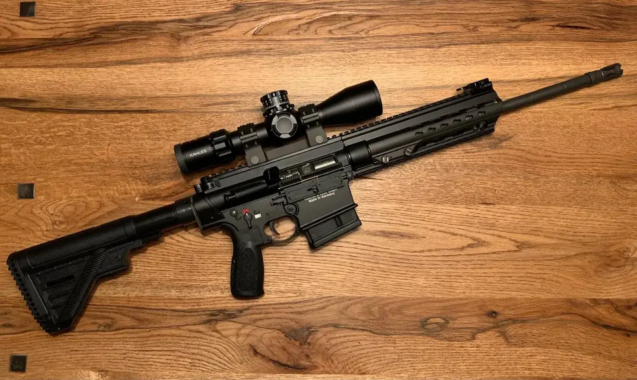 Un fusil HK MR308 noir avec lunette Kahles, pos&eacute; sur une table en bois.