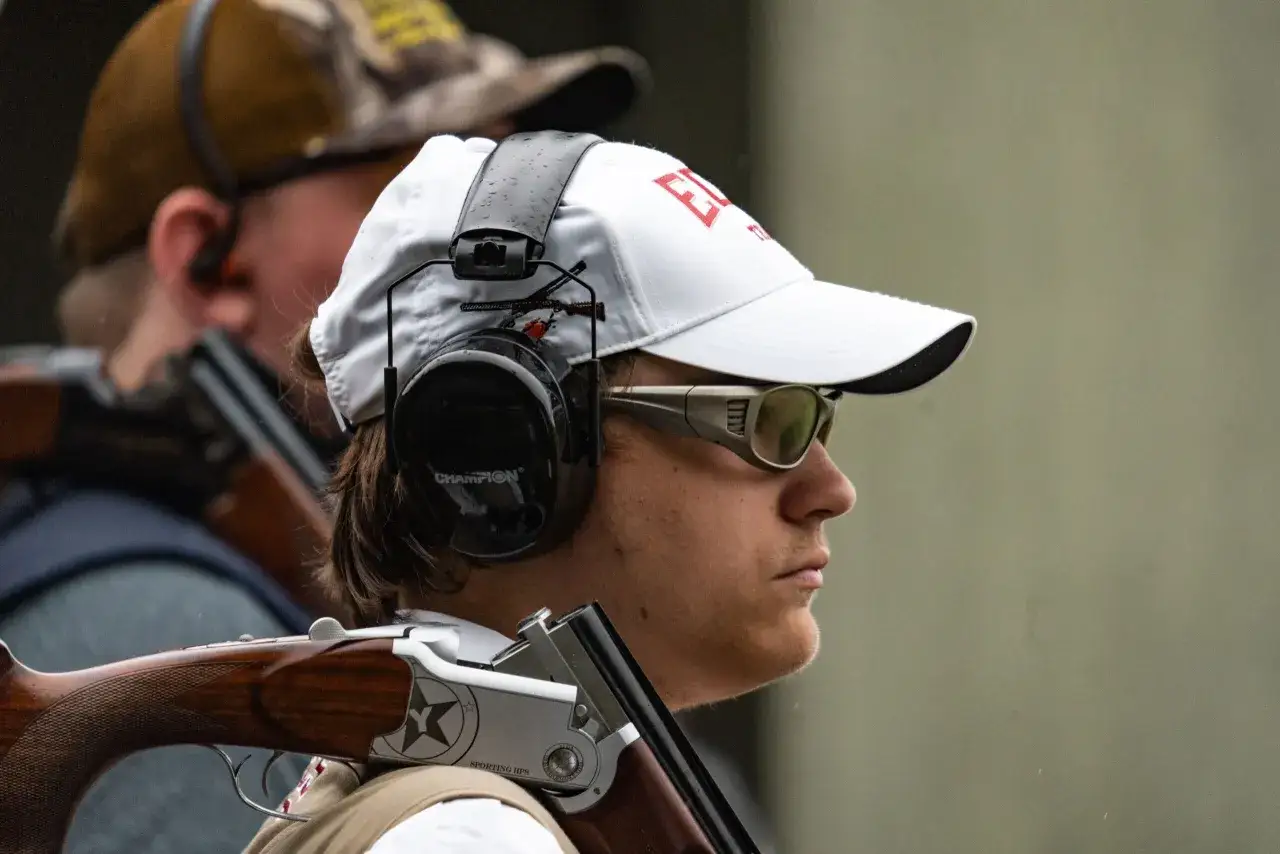 Un tireur concentr&eacute;, casquette blanche, lunettes de protection et casque anti-bruit, pr&ecirc;t &agrave; entendre le bruit de tir fusil de chasse.