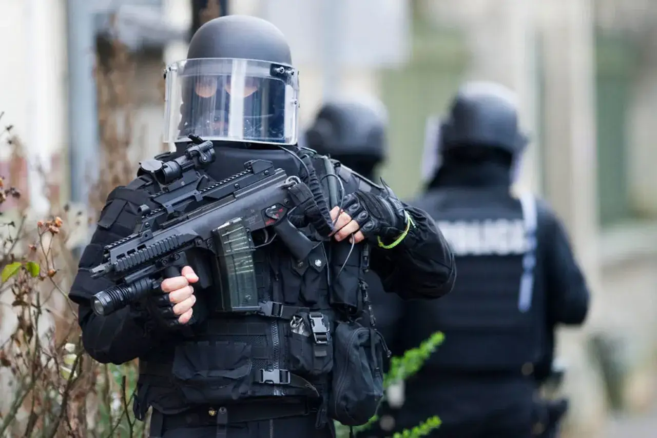 Un membre de la gendarmerie, &eacute;quip&eacute; d'un casque int&eacute;gral et d'un fusil d'assaut, se tient pr&ecirc;t.