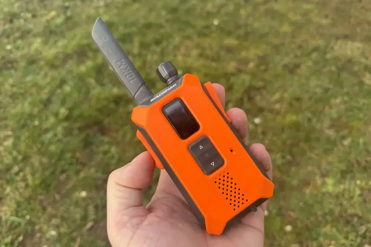 Talkie-walkie orange tenu dans une main, pr&ecirc;t pour la chasse. La fr&eacute;quence est r&eacute;gl&eacute;e pour une communication optimale.