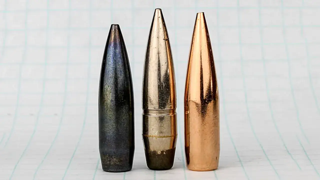 Trois balles de calibre 7,5x55, une noire, une argent&eacute;e et une cuivr&eacute;e, align&eacute;es sur un fond quadrill&eacute;.