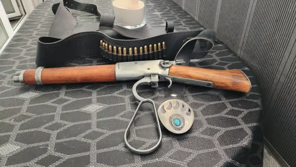Carabine à levier sous garde en bois et métal, avec ceinture de munitions et boucle d'ours.