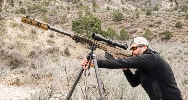 Un tireur d'élite ajuste son Barrett 50 munition sur un trépied, prêt à tirer dans un paysage désertique.