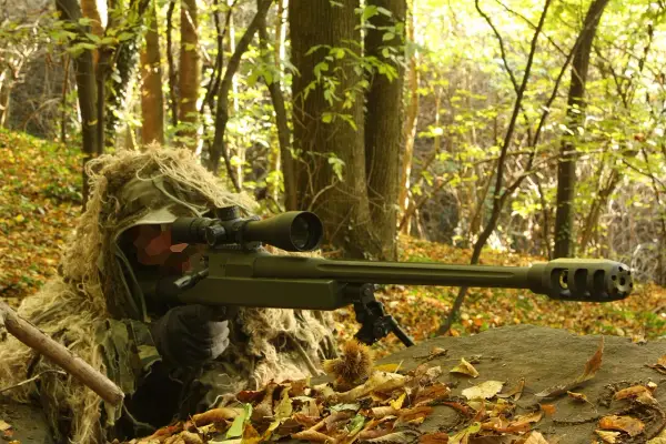 Un tireur d'élite camouflé dans les bois, tenant un fusil Macmillan.